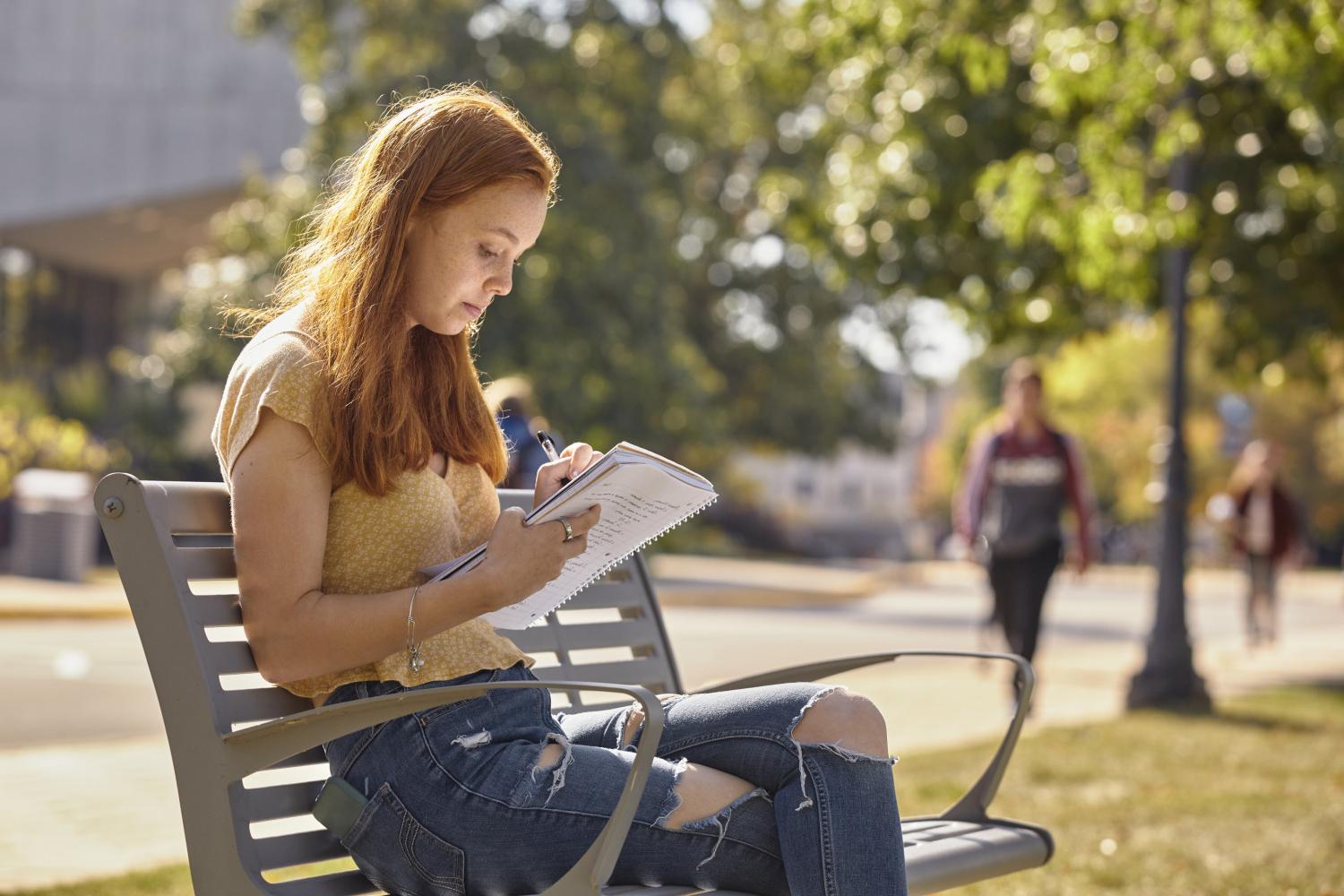 A <a href='http://c6m.stztjx.com'>BETVLCTOR伟德登录</a> student reads on a bench along Campus Drive.